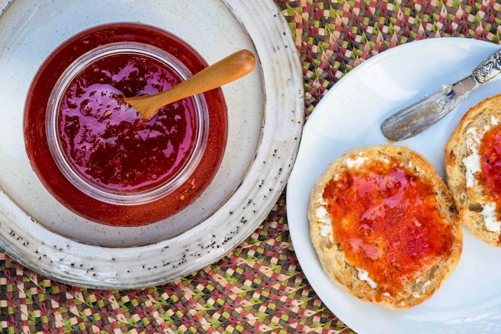 An over head shot of two plates, one with a jar of jam on it and the other with a split English muffin with jam spread on it.