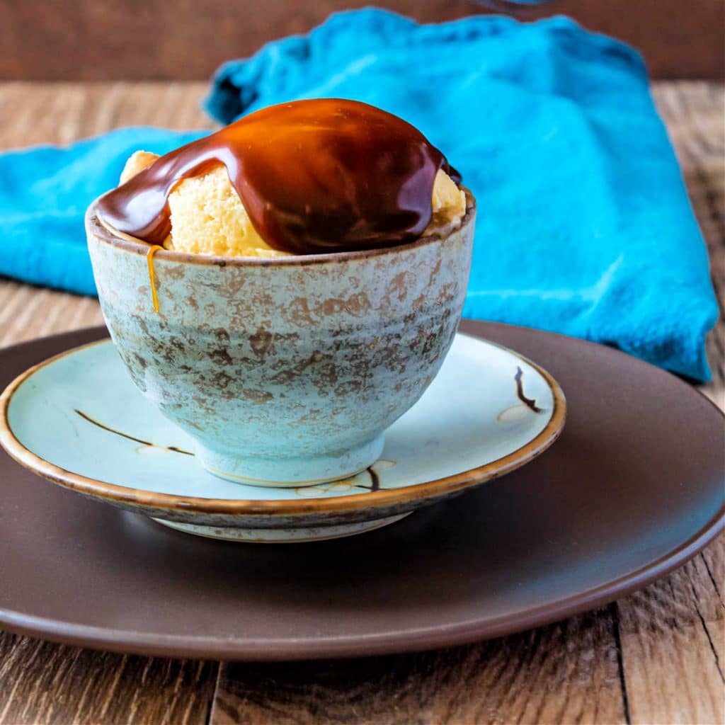 A dish of ice cream with butterscotch sauce on it.