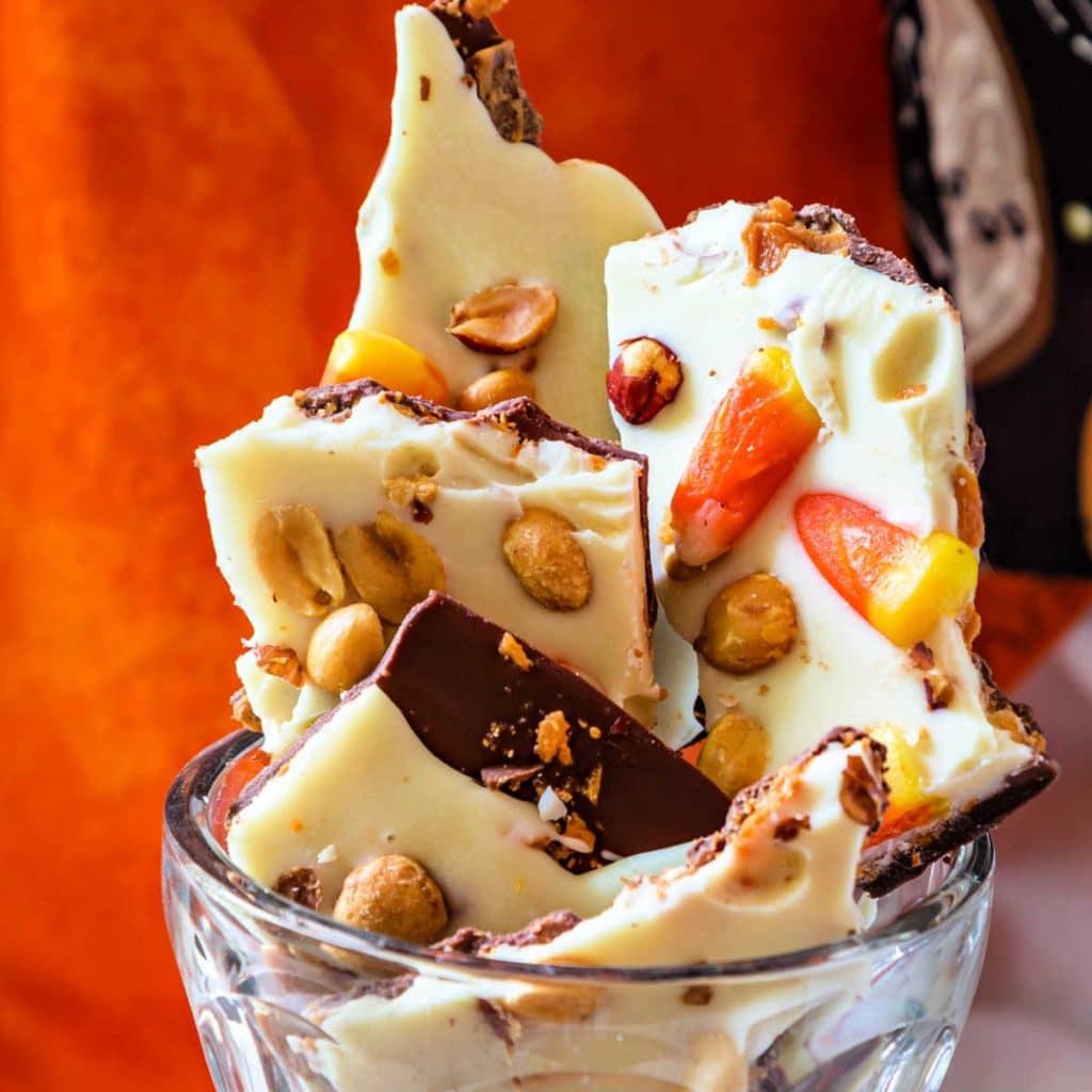 A close up of pieces of milk and white chocolate bark studded with crushed Butterfinger, peanuts, and candy corn.