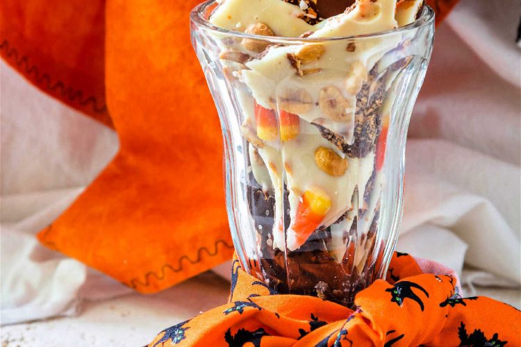 A tall glass with an orange napkin decorated with black cats tied around it and filled with candy.
