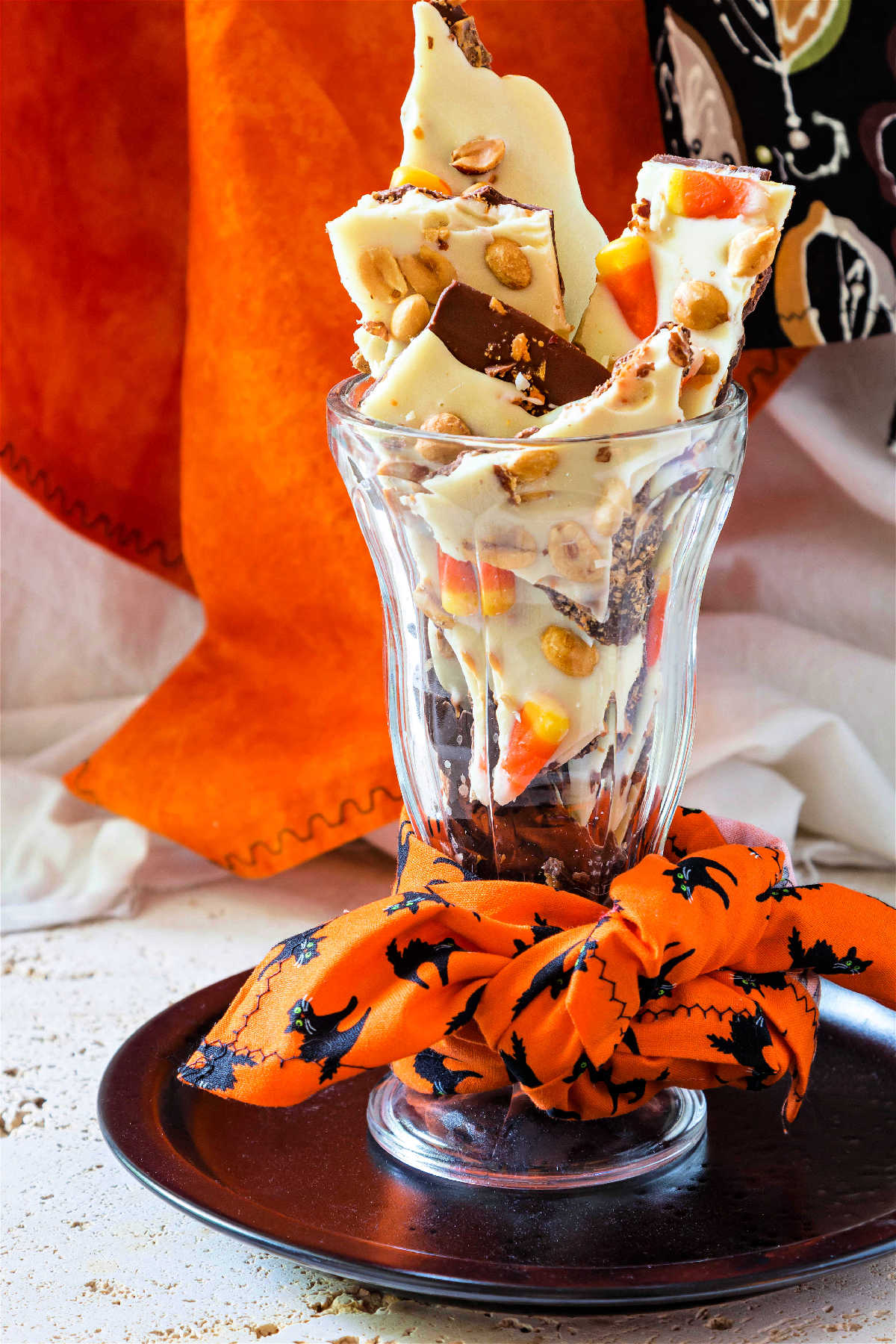 A tall glass with an orange napkin decorated with black cats tied around it and filled with candy.