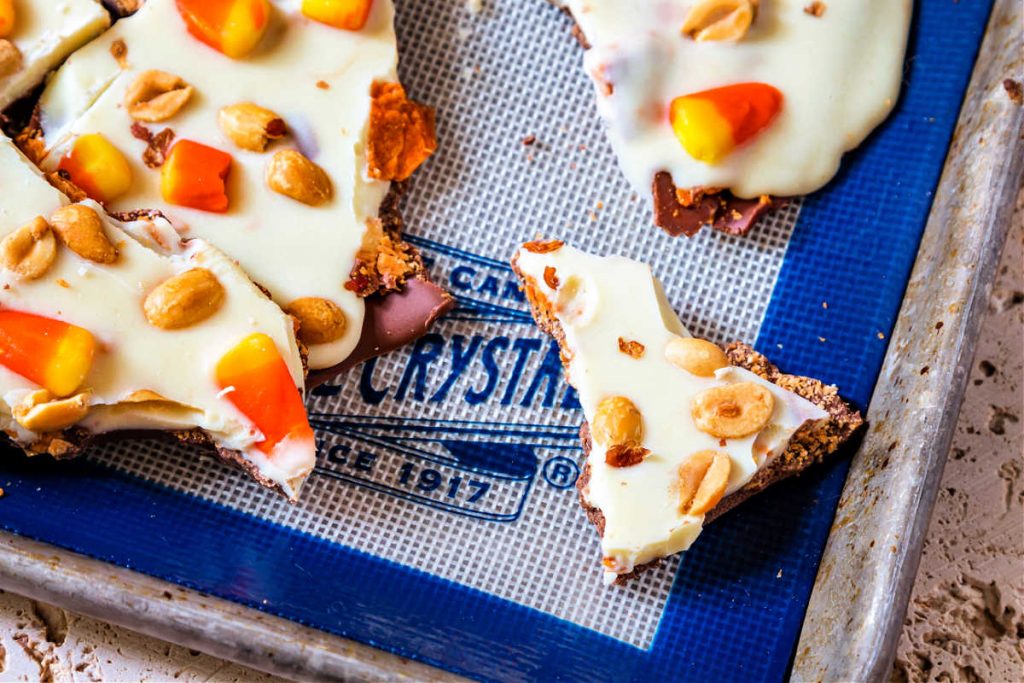 An overhead shot of pieces of candy bark with candy corn and peanuts on a white and blue baking mat.