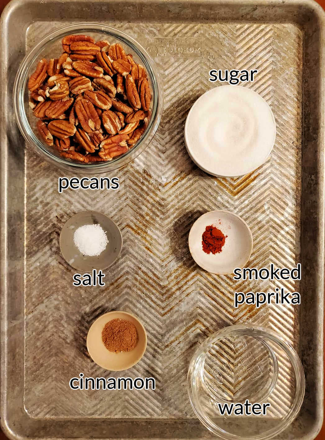 A collage of the ingredients for making cinnamon glazed nuts: pecans, sugar, salt, paprika, cinnamon, sugar, and water.