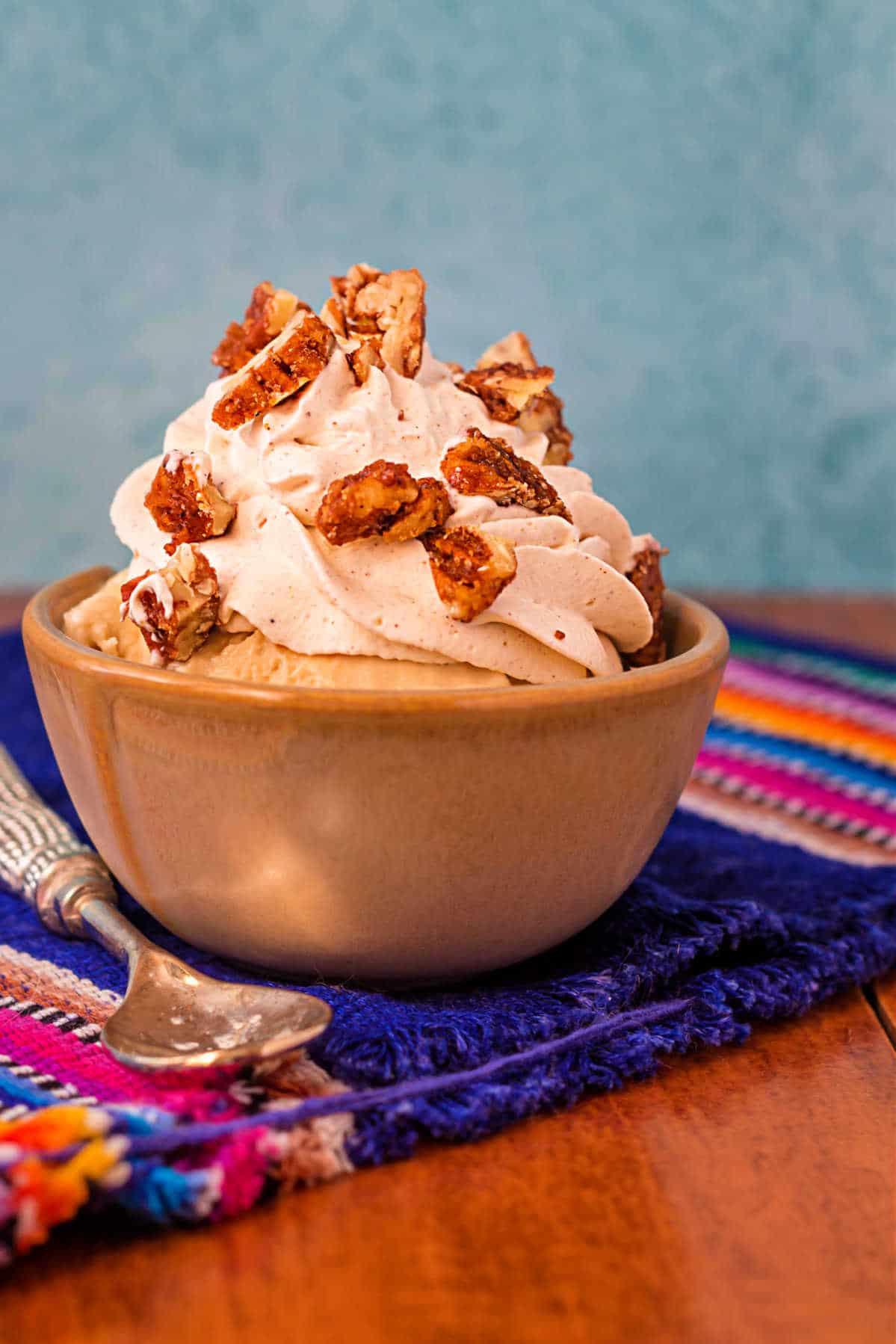 An ice cream sundae in a beige dish topped with spiced whipped cream and chopped cinnamon glazed nuts.