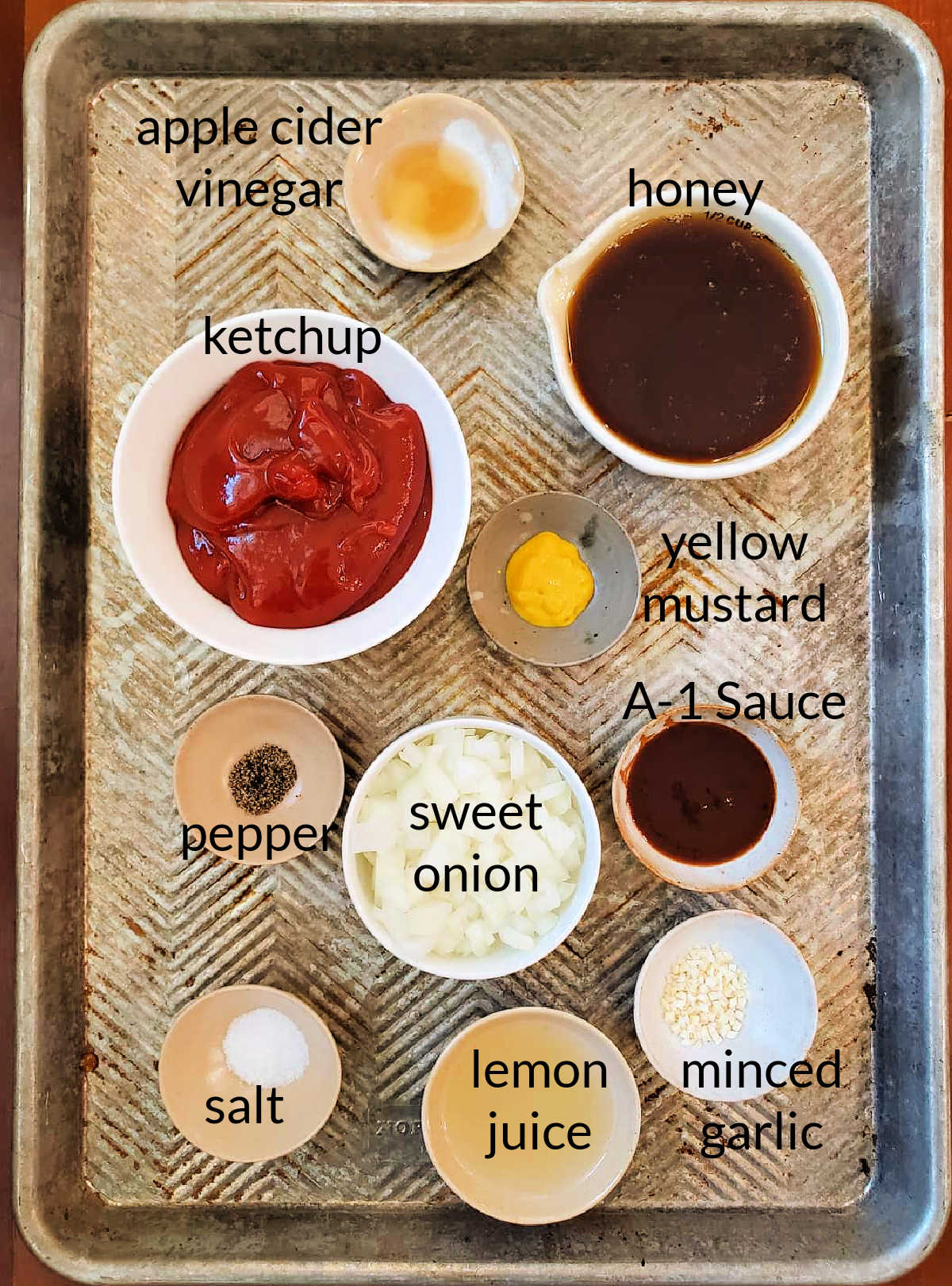 A collage of ingredients for making red sauce for cream cheese: vinegar, ketchup, honey, mustard, salt, pepper, onion, garlic, A1 sauce, and lemon juice.