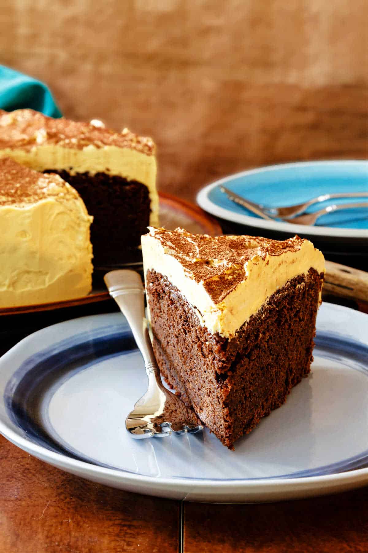 A slice of chocolate stout cake with a thick layer of caramel frosting on a blue plate.