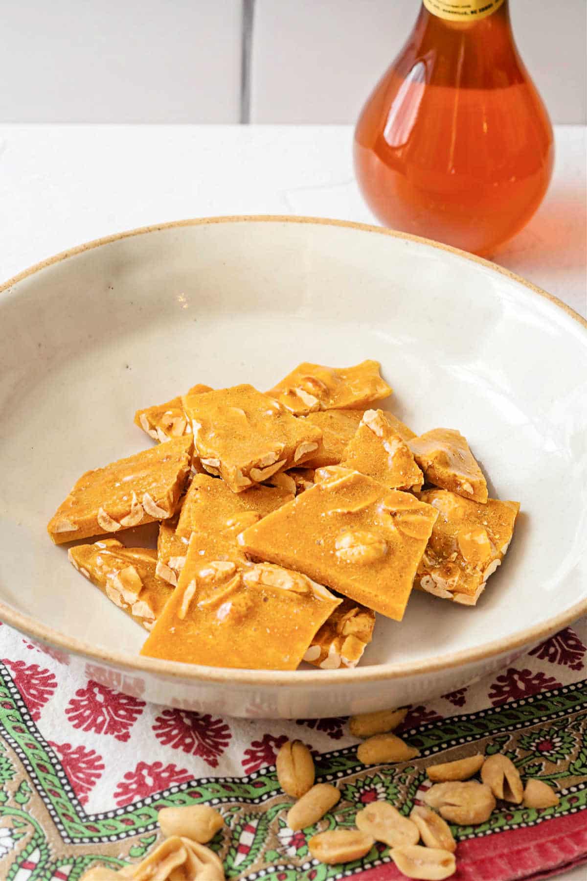 A beige bowl with pieces of honey peanut brittle in it.