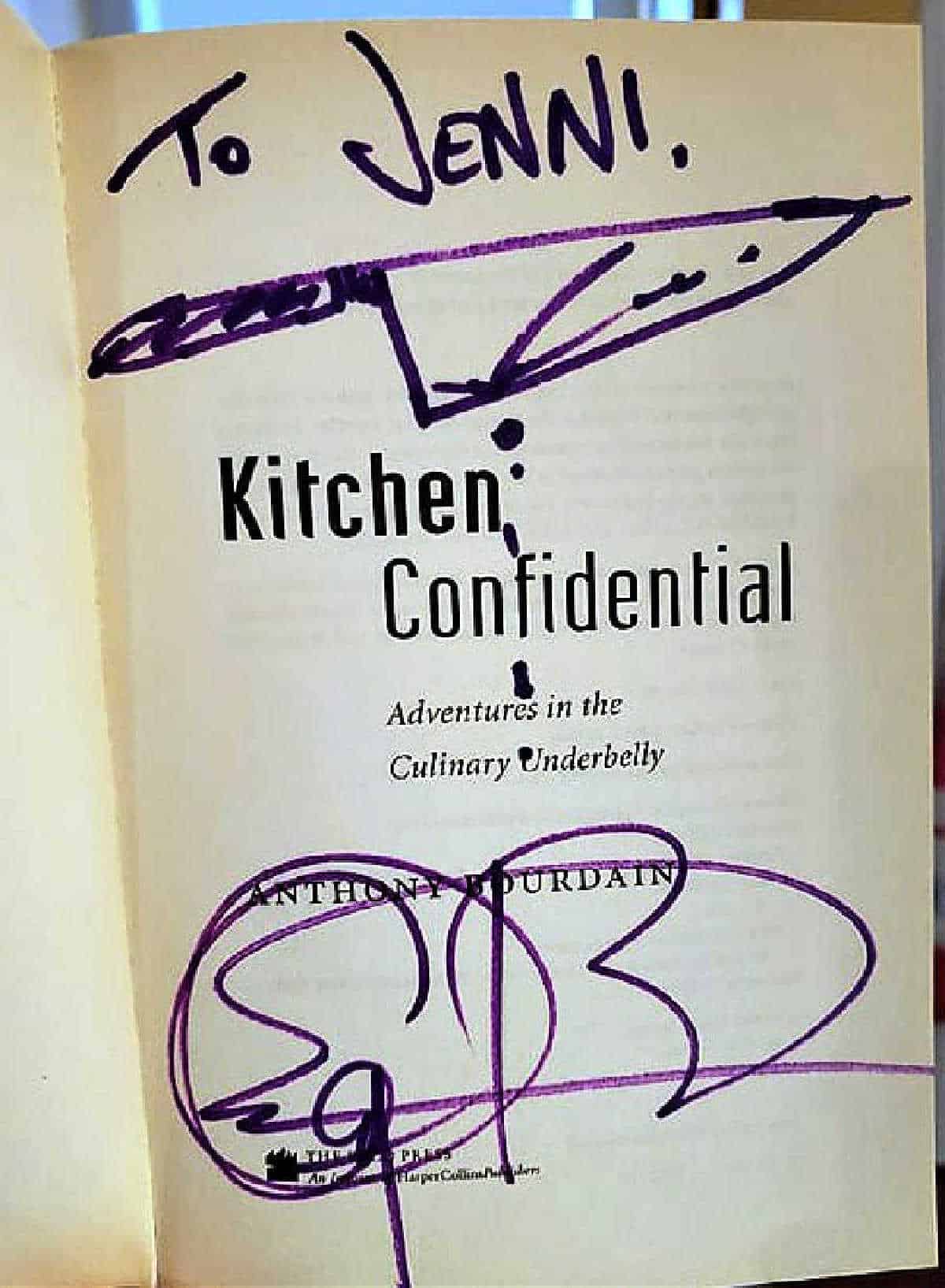 Inner title page of the book Kitchen Confidential, Adventures in the Culinary Underbelly, signed by Anthony Bourdain in purple marker: To Jenni, with a chef knife with "blood" dripping down and then his signature at the bottom of the page.