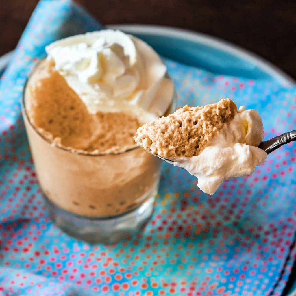 A glass filled with butterscotch mousse and a spoonful of mousse.