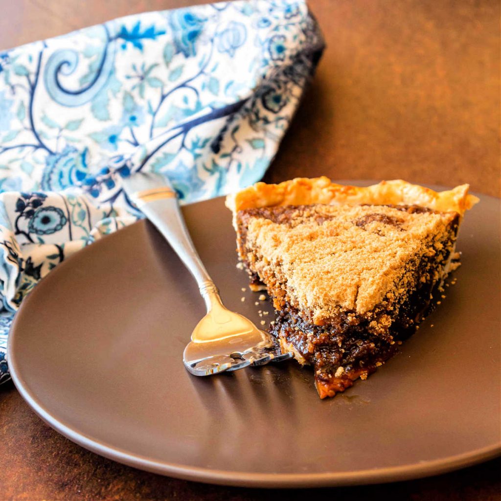 A slice of shoofly pie on a brown plate with a fork and a blue napkin.