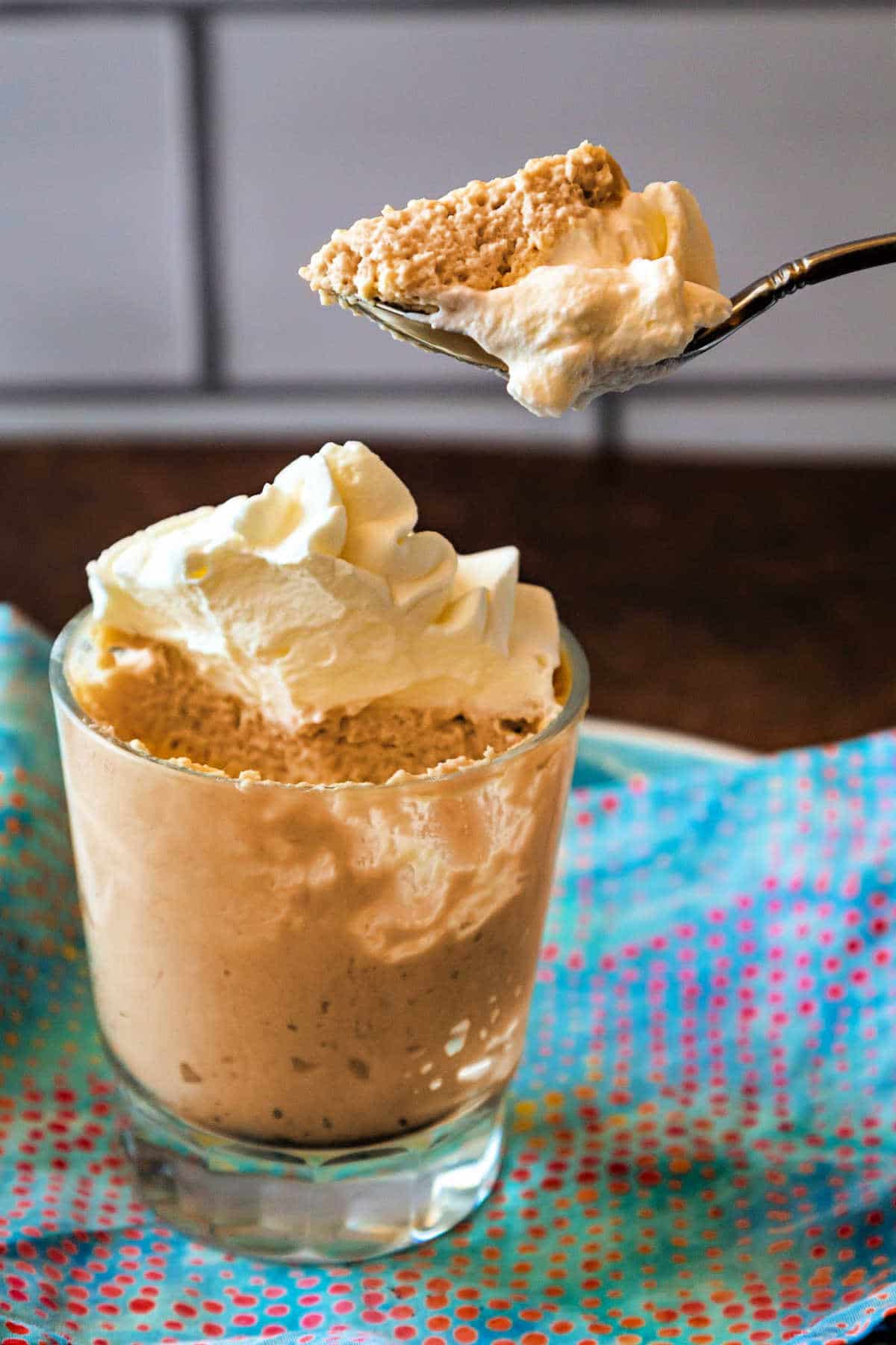 A dish of butterscotch mousse topped with whipped cream with a bit of mousse on a teaspoon.