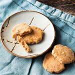 One whole pecan shortbread and one broked in two on a small plate. Two whole pecan sandies are next to the plate on a blue napkin.