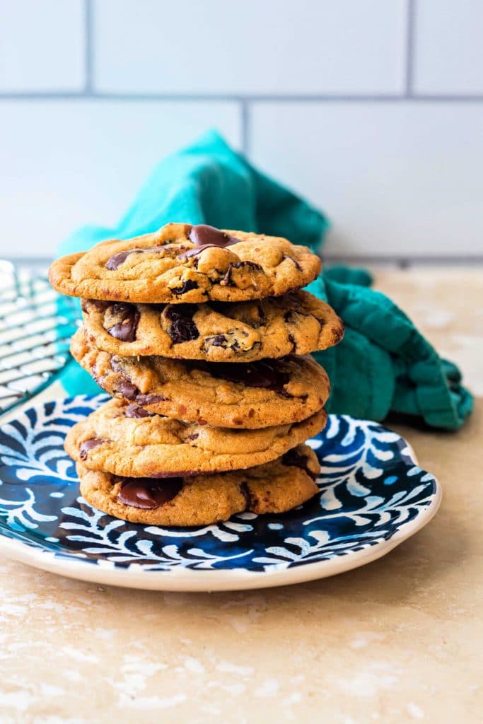 A blue plate with a stack of five chocolate chip cookies on it.