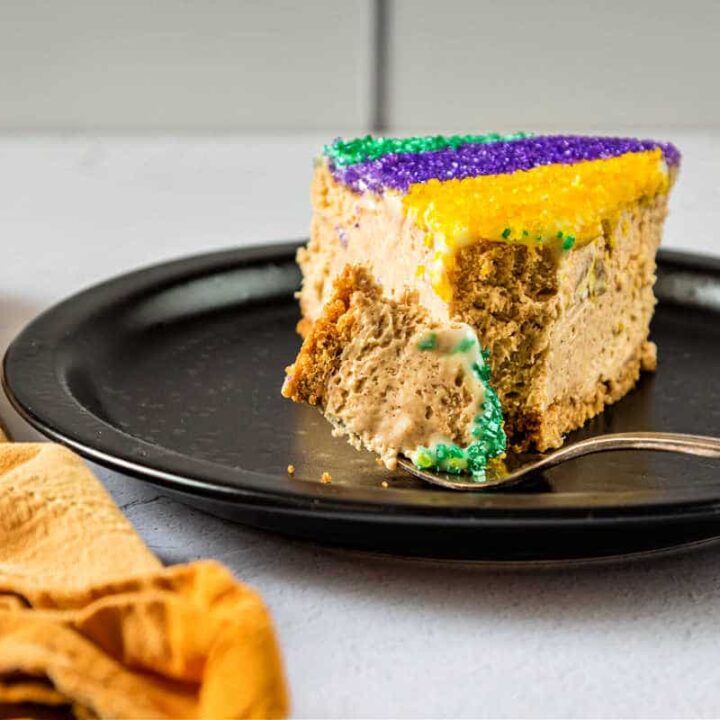 A slice of cinnamon cheesecake decorated with colored sugar on a black plate.