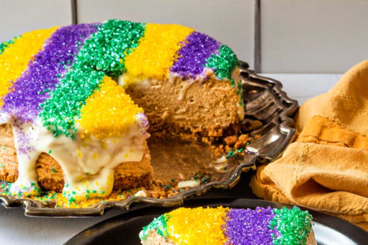 A slice of King Cake cheesecake on a black plate with the rest of the cheesecake in the background.