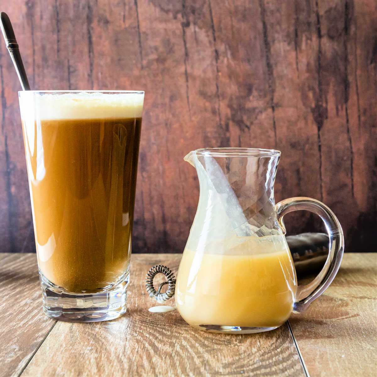 A glass with white chocolate mocha and a glass pitcher of white chocolate coffee sauce.