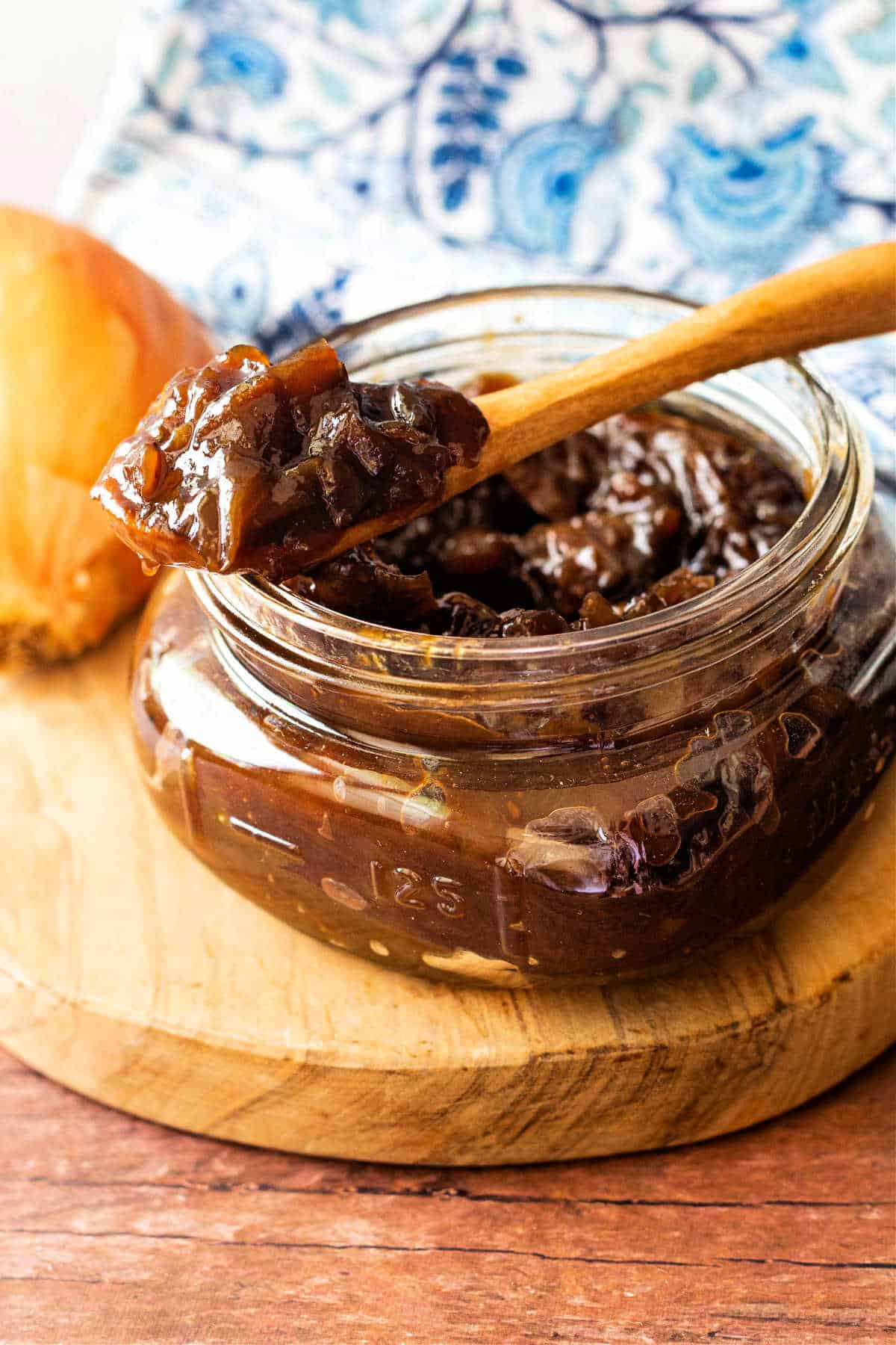 A glass jar containing onion jam iwth a wooden spoon in it.
