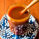 A jar of deep orange-amber sauce on a blue patterned plate.