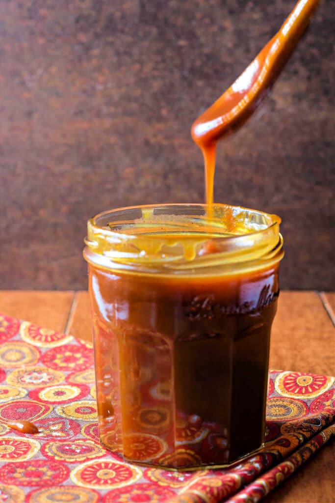 A wooden spoonful of pumpkin caramel sauce being drizzled back into the jar.