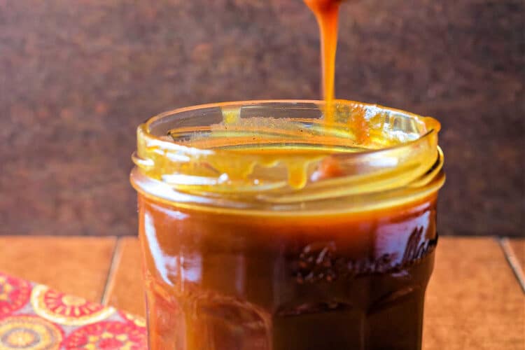 A wooden spoonful of pumpkin caramel sauce being drizzled back into the jar.