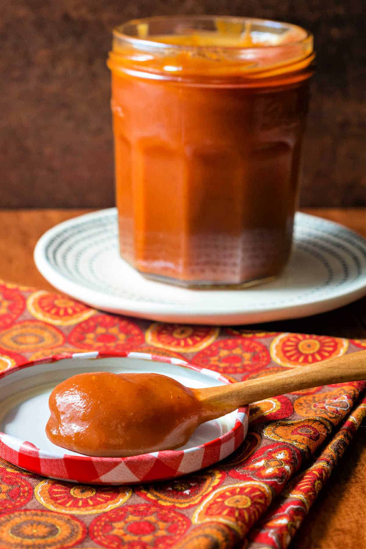 A full jar of deep amber caramel sauce with a spoonful of the sauce resting on the lid of the jar.