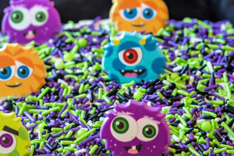 Top of a sheetcake decorated with green, purple, and black sprinkles and cute plastic monsters.