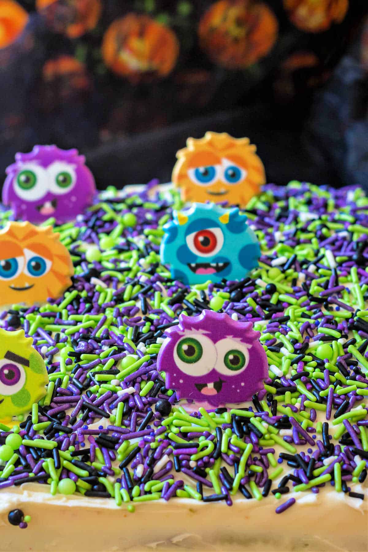 Top of a sheetcake decorated with green, purple, and black sprinkles and cute plastic monsters. 