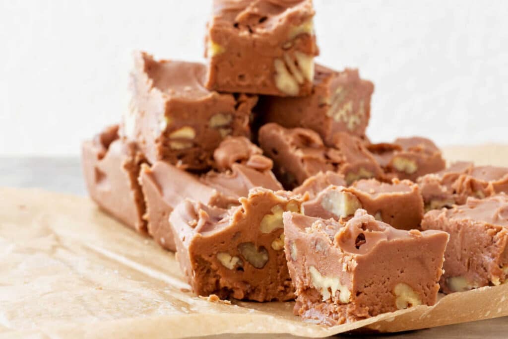 A stack of cubes of fudge with nuts on beige parchment paper.