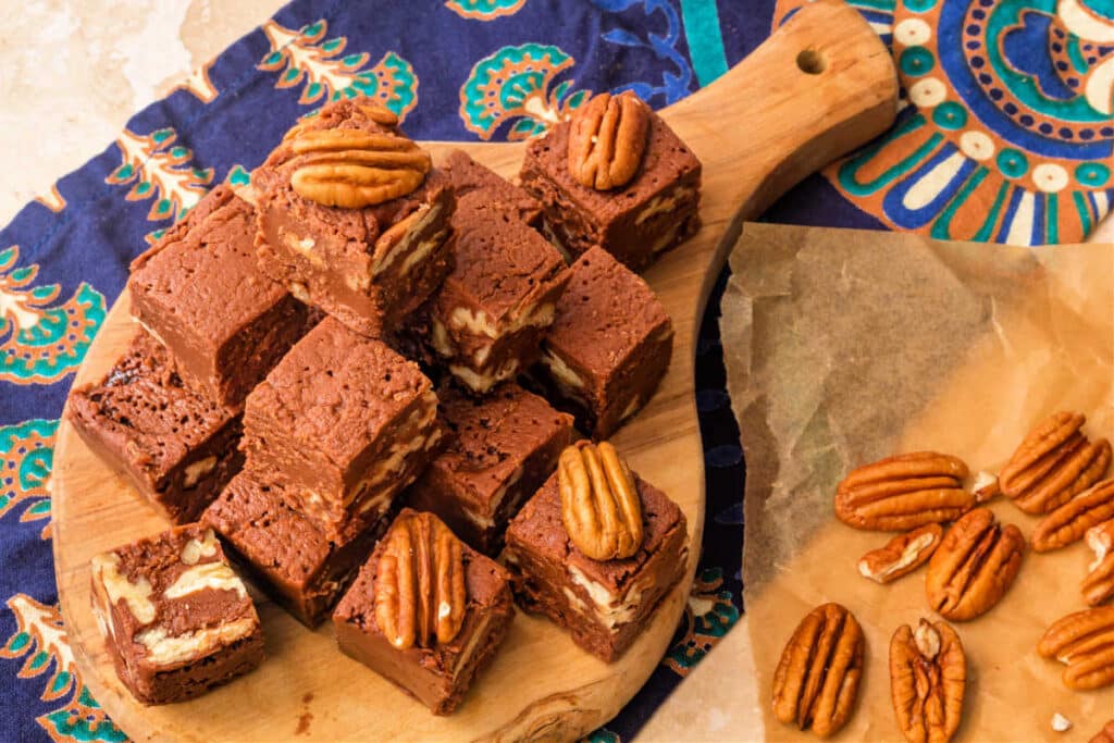 Stacked old-fashioned fudge with pecans on a small cutting board.