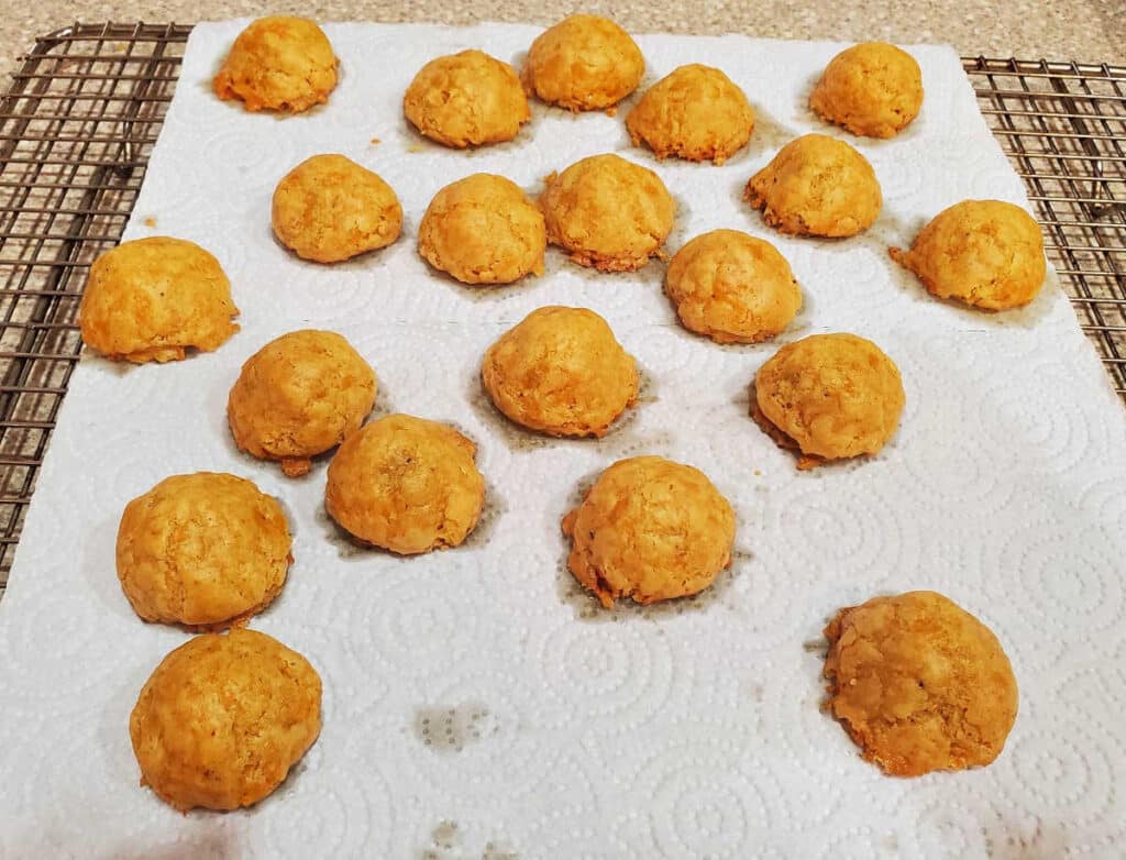 Baked cheese olive balls on a white paper towel.  There is a little bit of fat soaked into the towel around each puff.