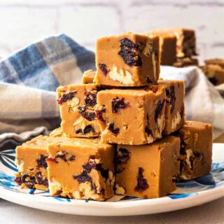 A small plate of squares of brown sugar fudge piled up on it with a blue plaid napkin in the background.