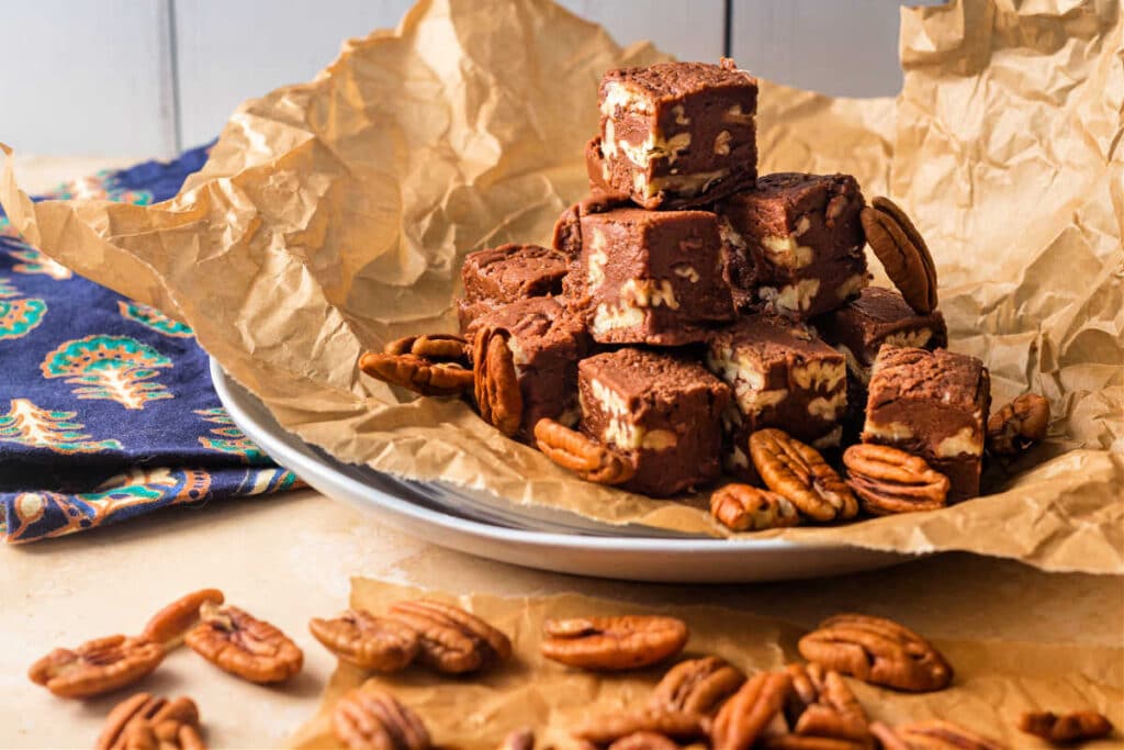 A plate lined with parchment and piled with old-fashioned fudge with pecans in it.