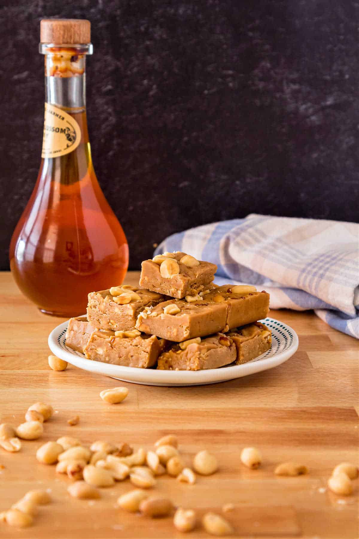 A small plate with a pile of peanut butter fudge on it. There's a jar of honey in the background and peanuts scattered in front of the plate.