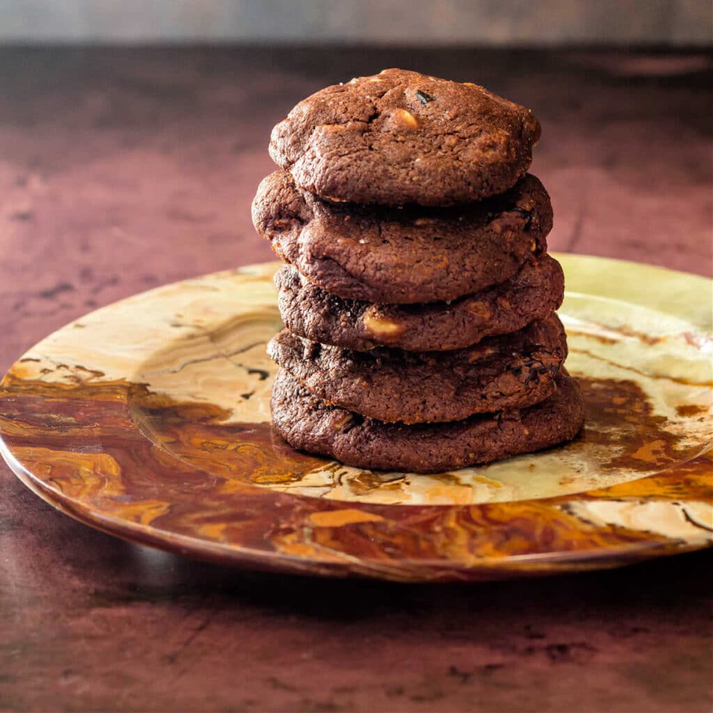 A brown plate with five brown cookies stacked on top of each other.