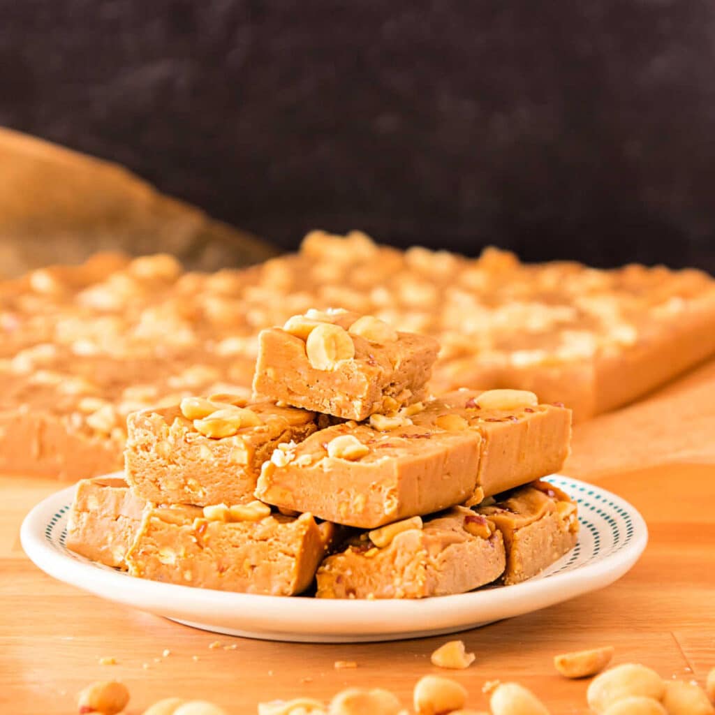 A plate of fudge in front of a slab of the same fudge in the background shot on a wooden surface.