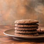 A stack of brown cookies on a brown plate shot on a wooden background with a worn bronze backdrop.
