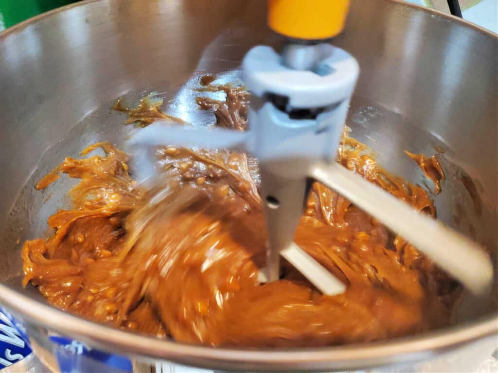 A close-up view into a mixer bowl showing the paddle beating fudge to cool it down and help it to thicken.