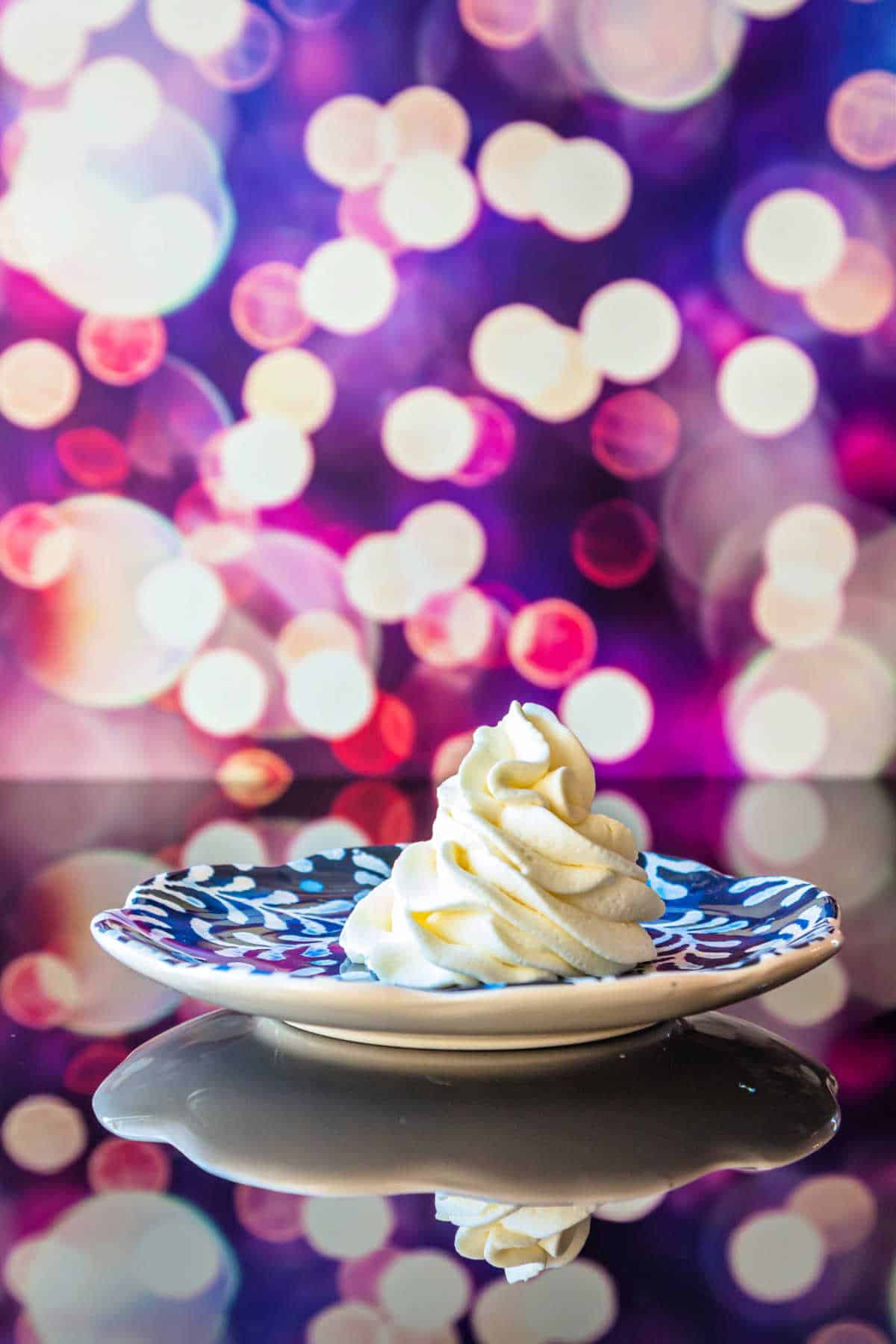 Piped whipped cream on a blue-patterned plate shot against a background of fuscia and purple with twinkling lights.