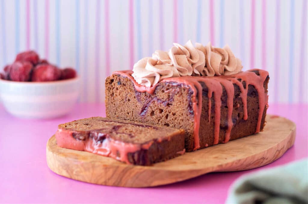 A horizontal shot of a sliced strawberry pound cake on a wooden board with a small bowl of strawberries in the background.