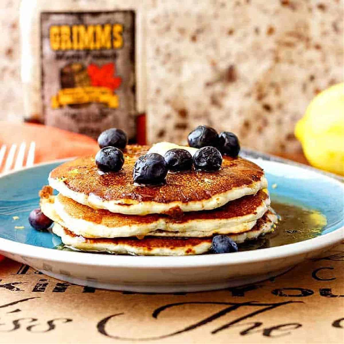 A close shot of stack of three pancakes on a blue plate topped with a pat of butter and fresh blueberries.