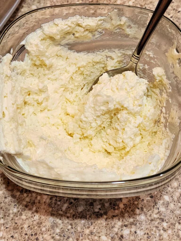 A close up of a glass container of whipped cream with a spoon in it. The texture is a bit thick and uneven-looking.
