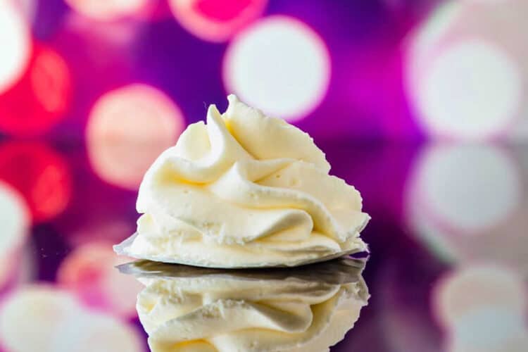 A "poof" of piped whipped cream on a reflective surface with purple and fuschia lights in the background.