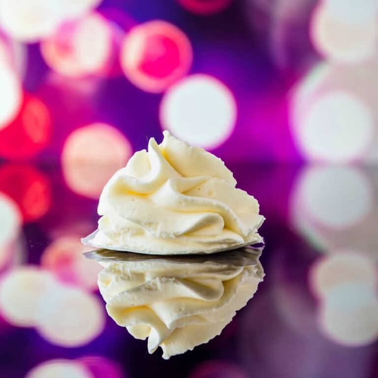 A "poof" of piped whipped cream on a reflective surface with purple and fuschia lights in the background.