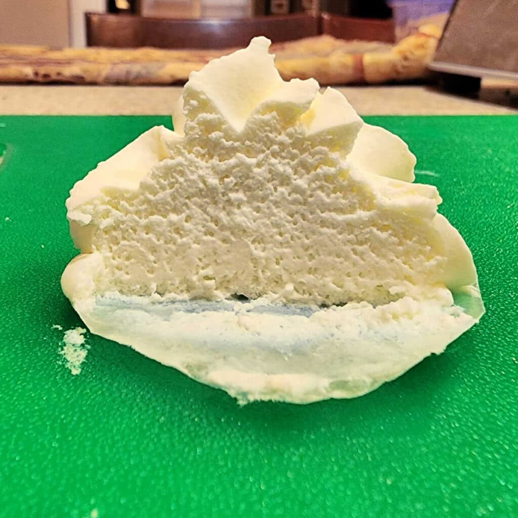 Piped whipped cream sliced in half to show the texture after being piped 36 hours before. The texture is mostly smooth and just a little bit spongy.