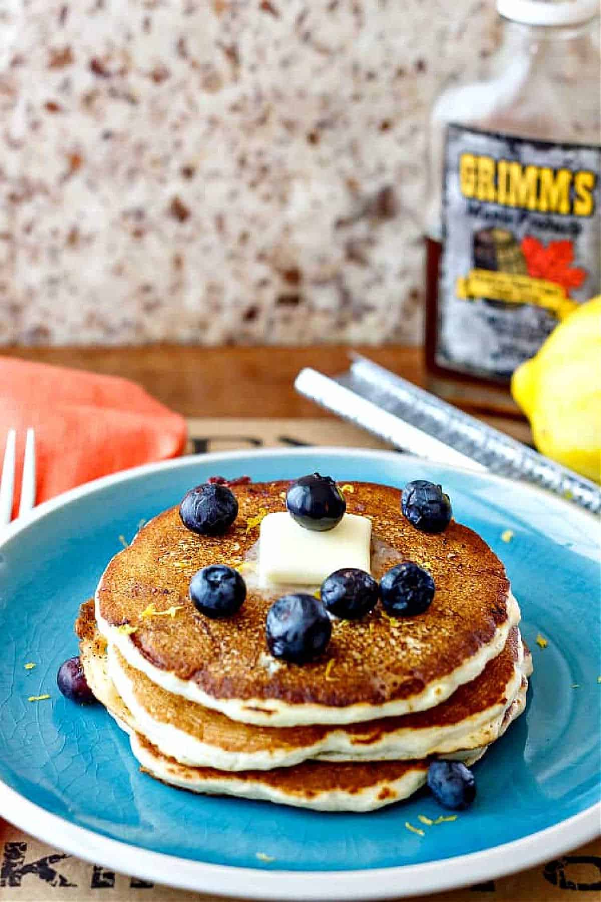 A stack of 3 pancakes for one on a blue plate with a pat of butter and fresh blueberries.