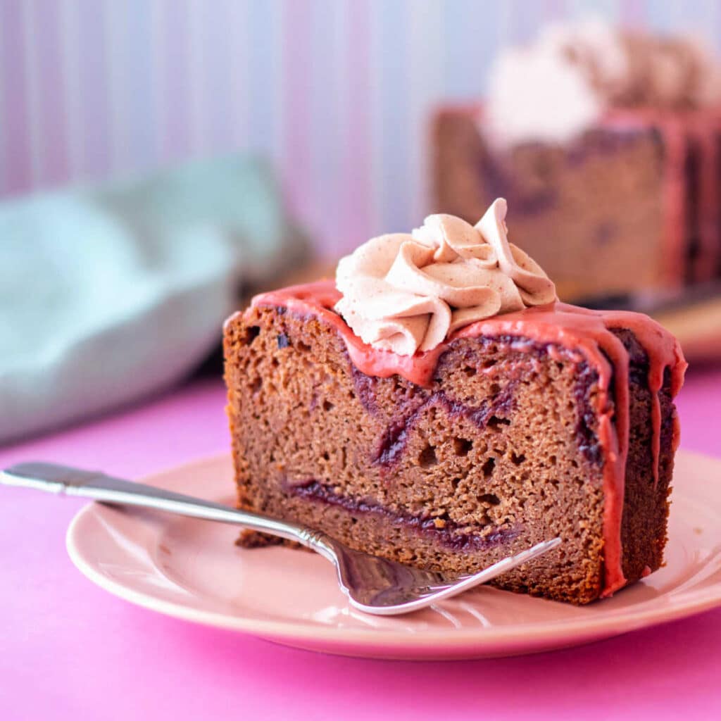 An upright slice from a loaf cake on a pink plate with a fork.