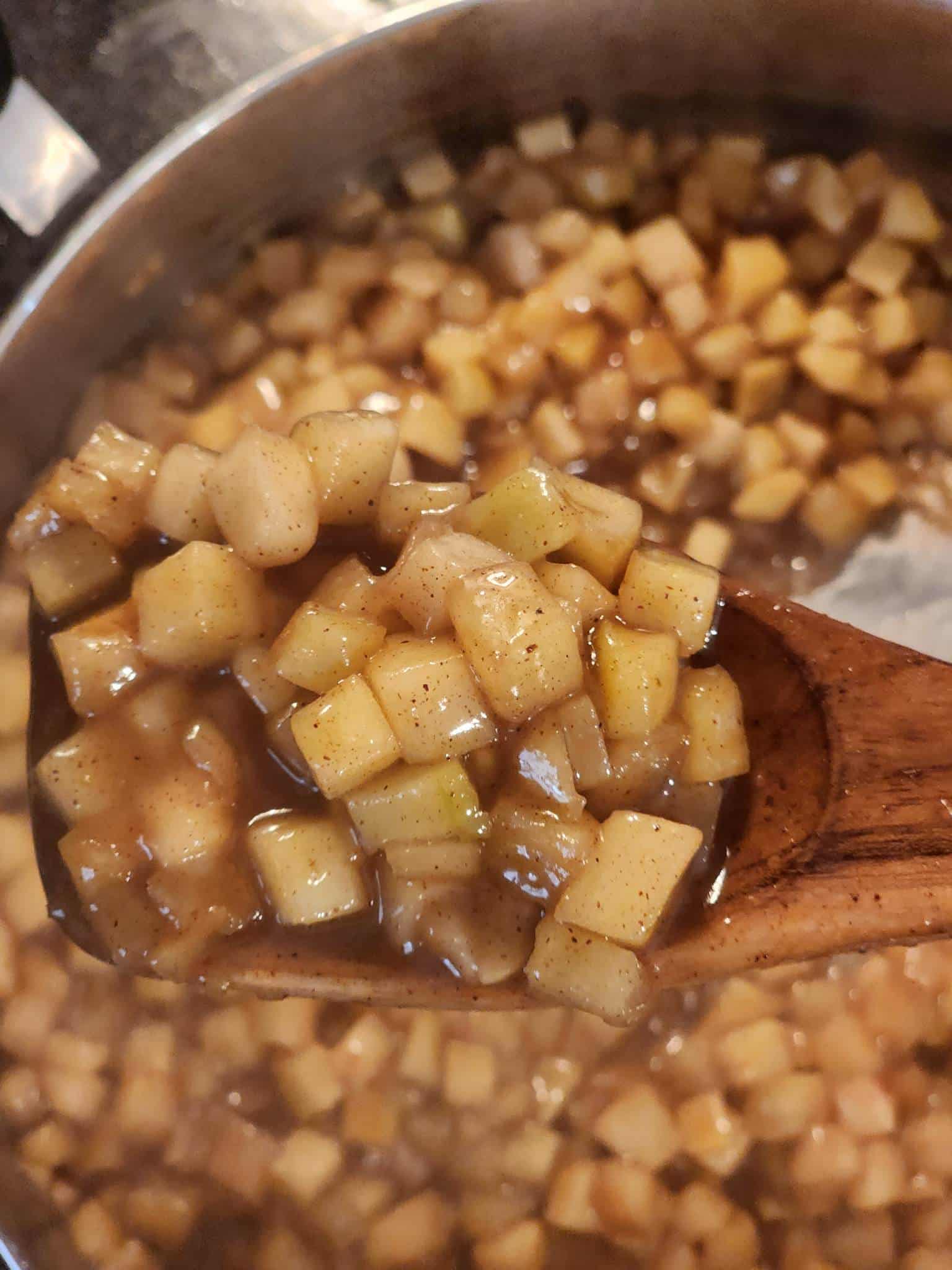 An overhead shot of a wooden spoonful with apple compote on it showing small diced apples coated in spice-flecked sauce.