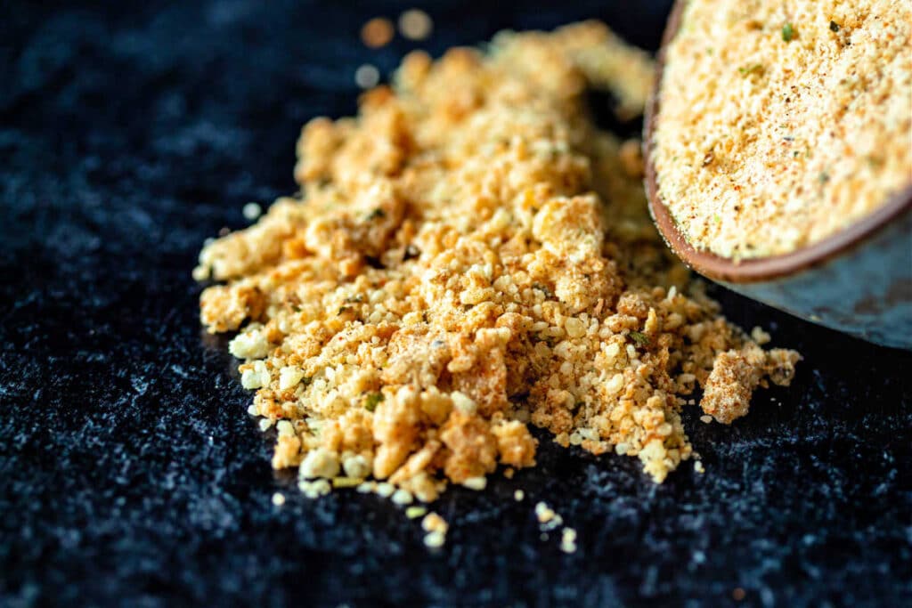 A close-up of grated Parmesan cheese mixed with spices tipping out of a small bowl and onto a black surface.