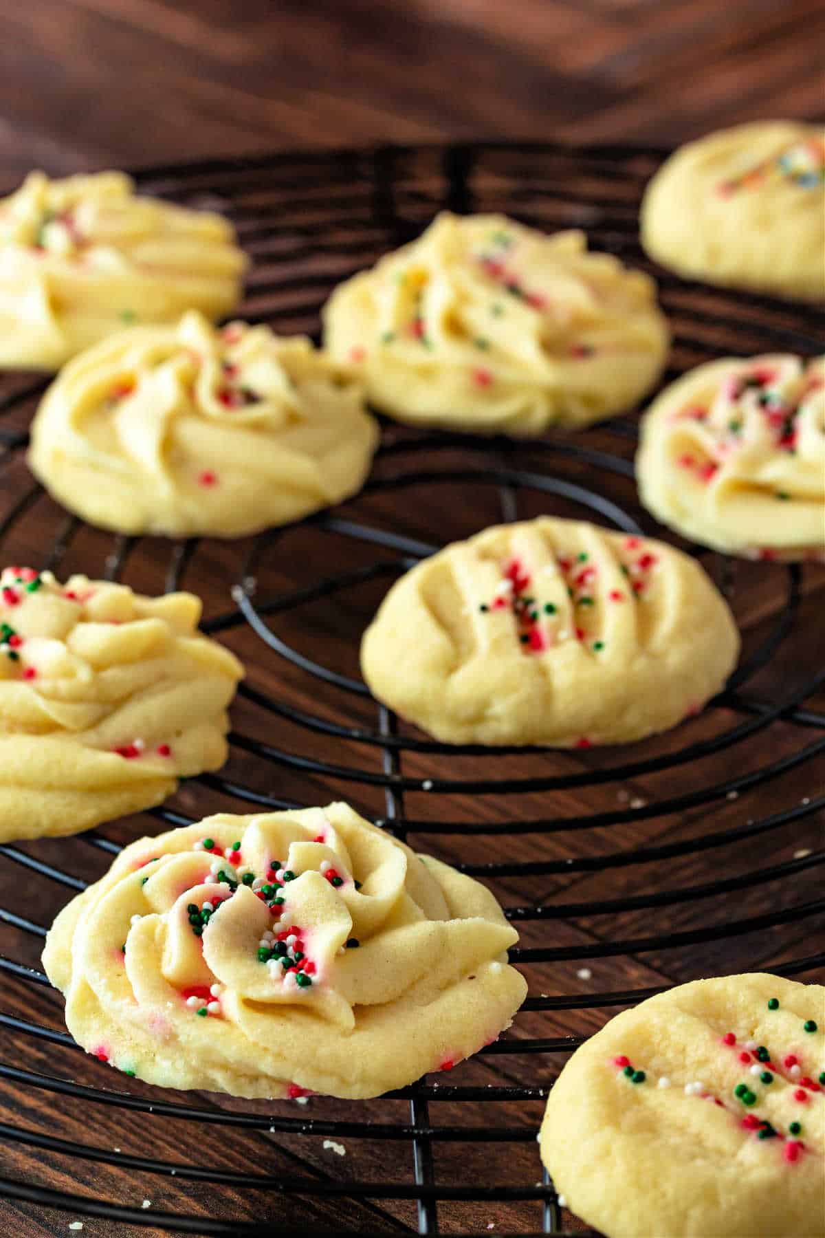 Piped whipped shortbread cookies with Christmas sprinkles cooling on a rack.