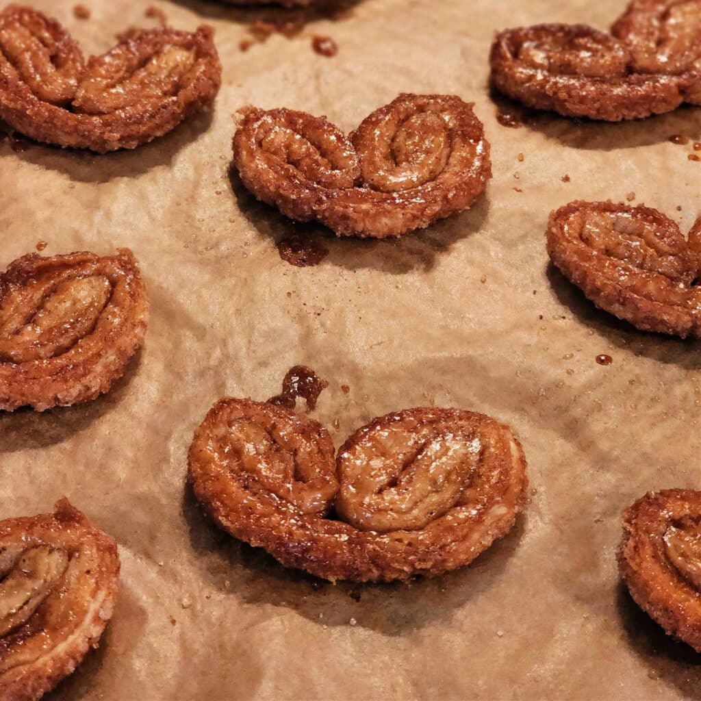 A close up of deep, golden-brown palmier cookies on a baking sheet.